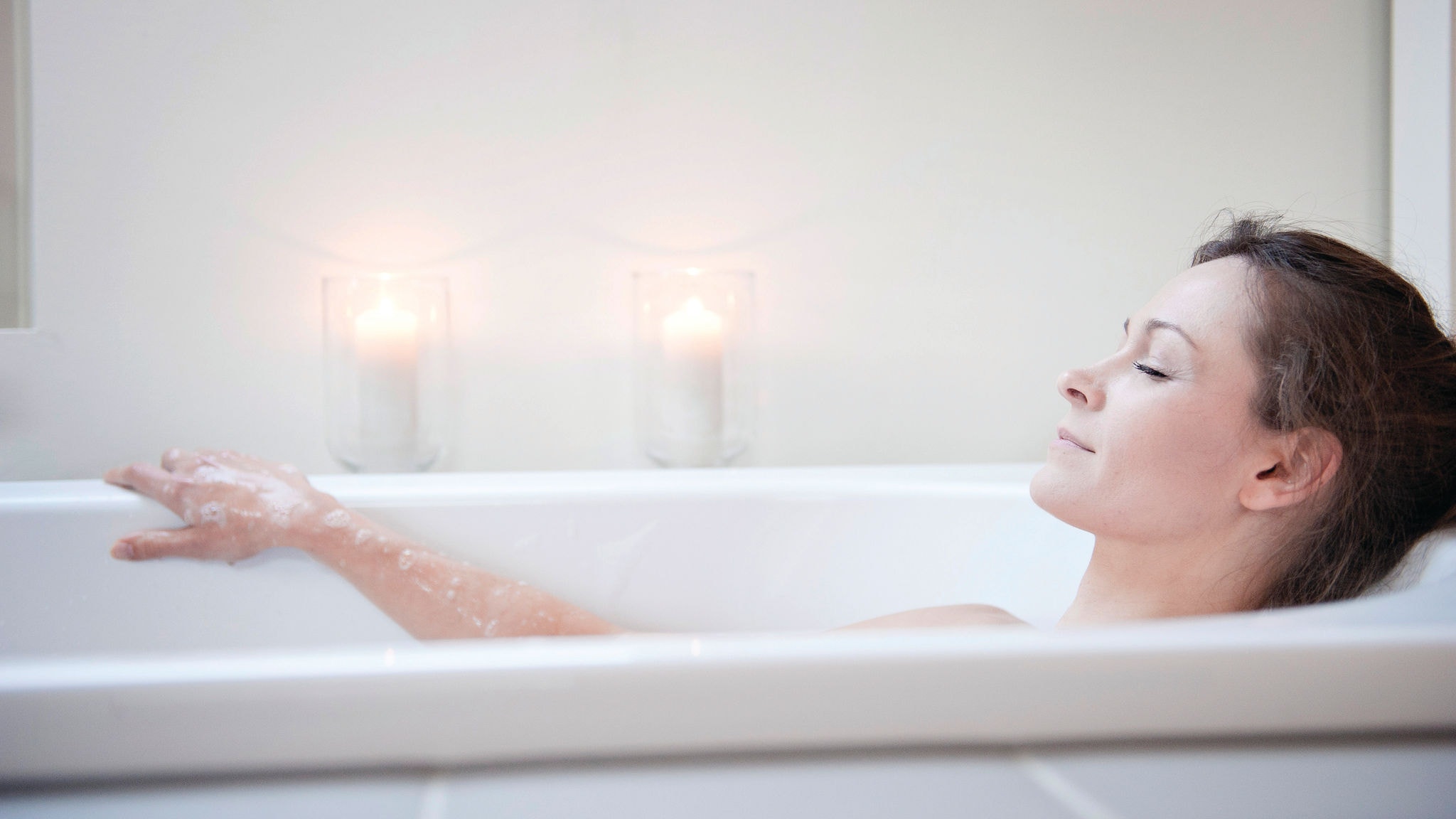 Eine Frau entspannt sich in einer Badewanne mit durch erneuerbare Energie über eine Daikin Brauchwasserwärmepumpe erwärmtem Wasser