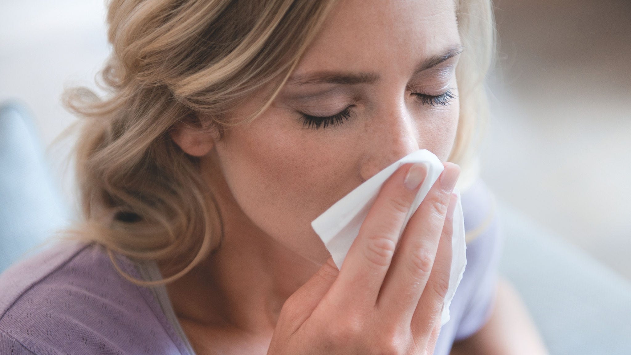 Frau putzt sich aufgrund einer Pollenallergie die Nase