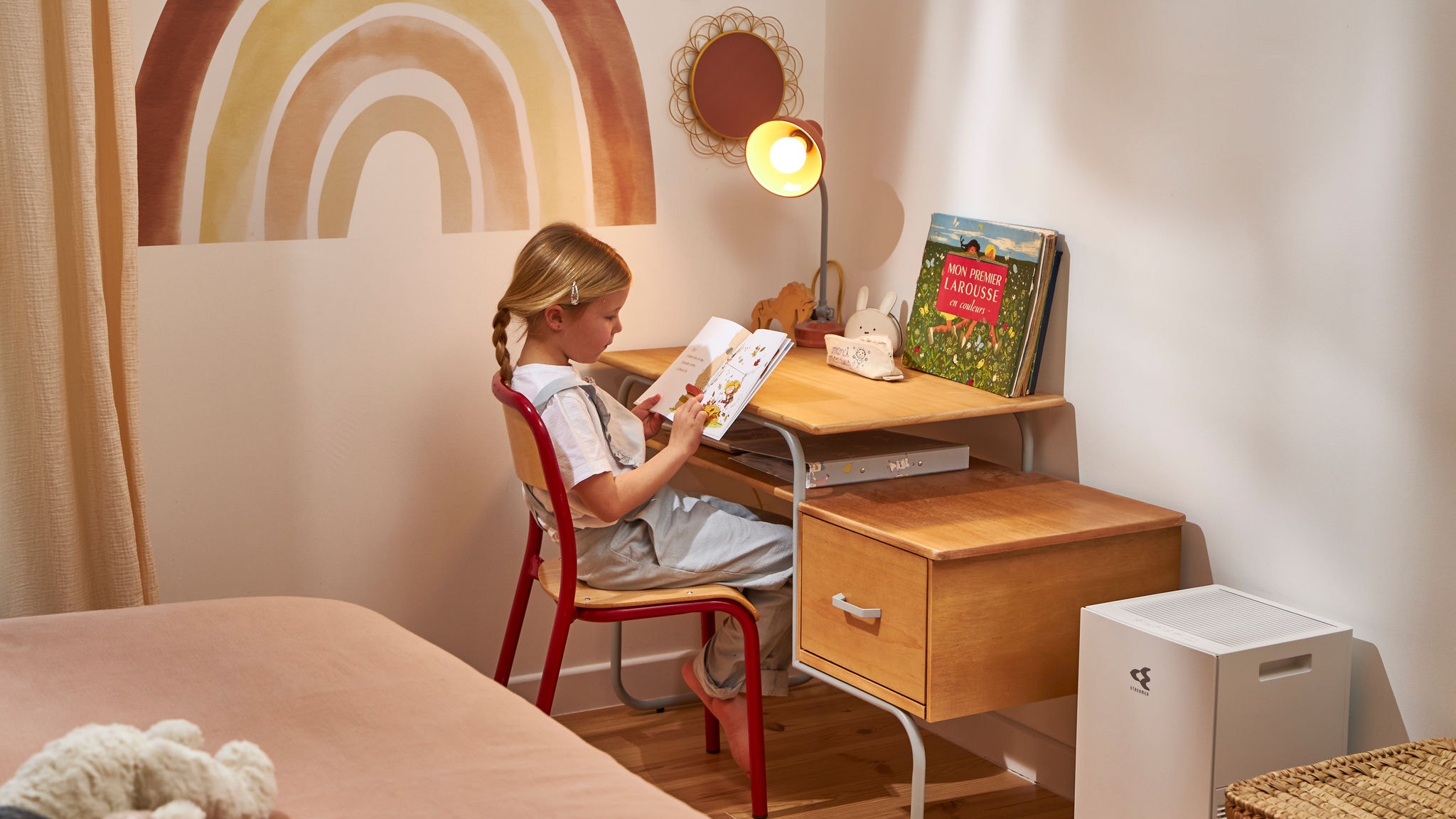 Ein Kind liest ein Kinderbuch. Dank des Luftreinigers neben ihrem Schreibtisch ist die Luft sauber.