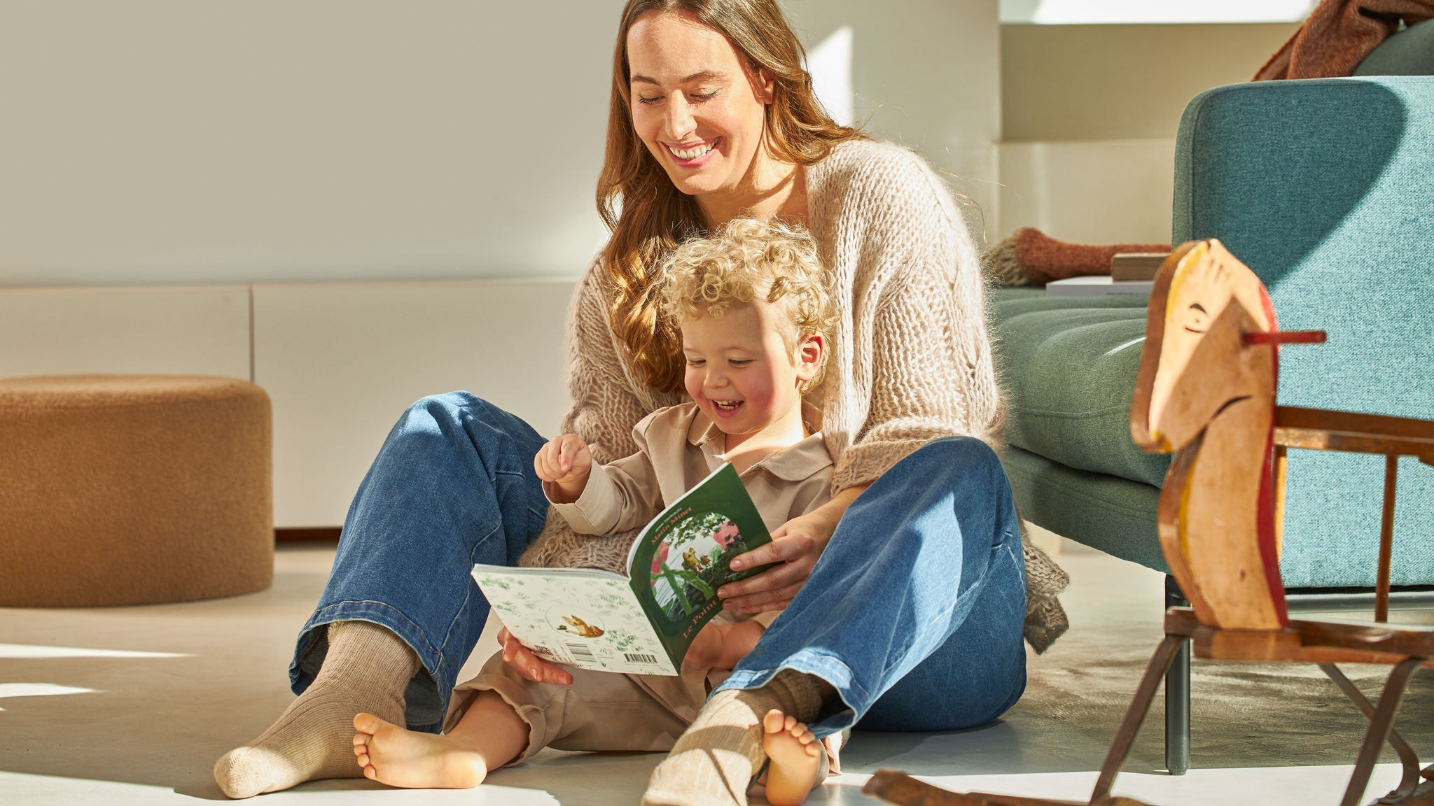 Eine Mutter liest mit ihrem Kleinkind ein Buch, in ihrem Zuhause auf dem von Daikin Altherma beheizten Fußboden sitzend