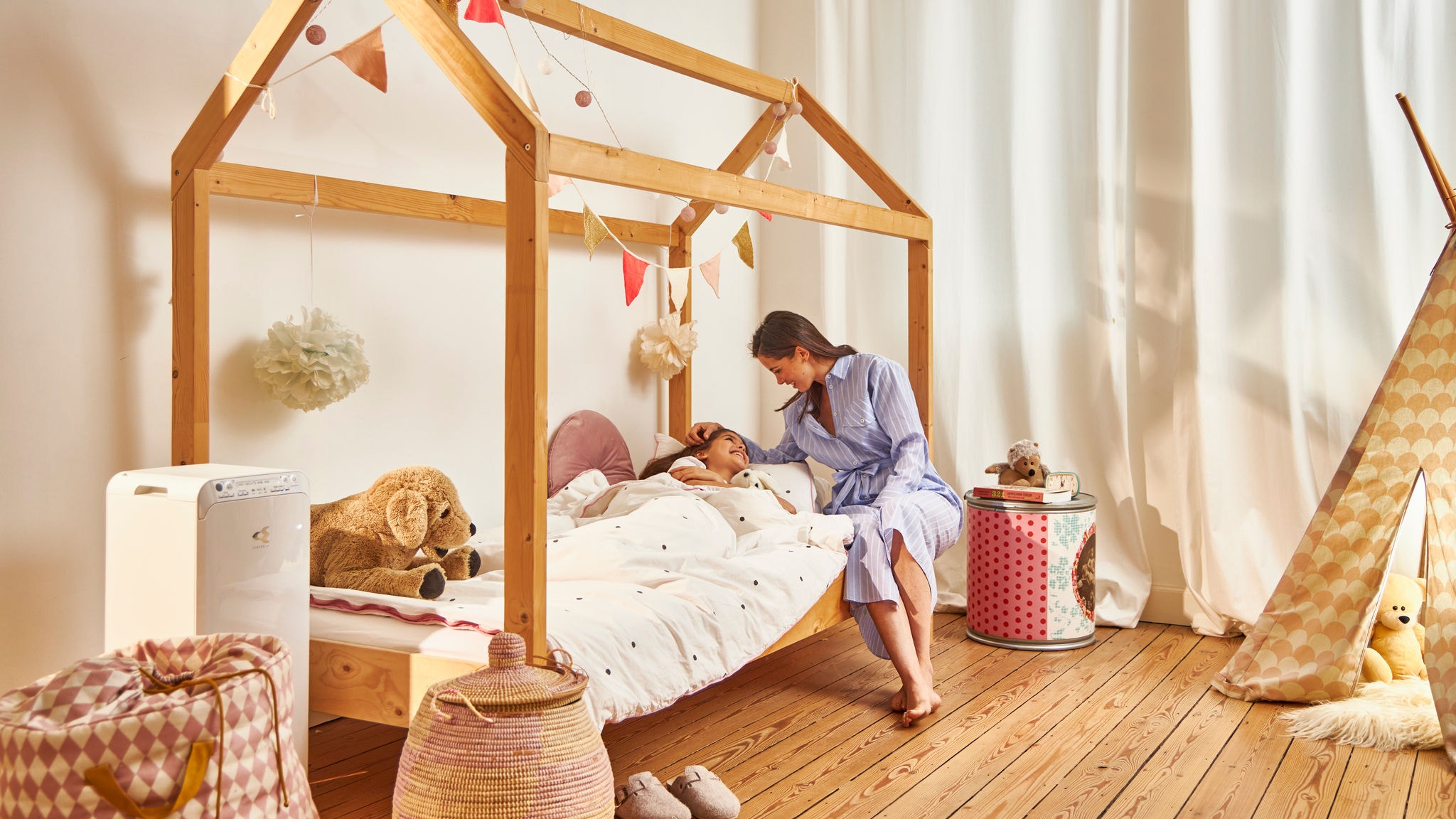 Mutter bringt ihre Tochter in ihrem Kinderzimmer zu Bett, dank eines Luftreinigers bei Raumluft optimaler Luftqualität