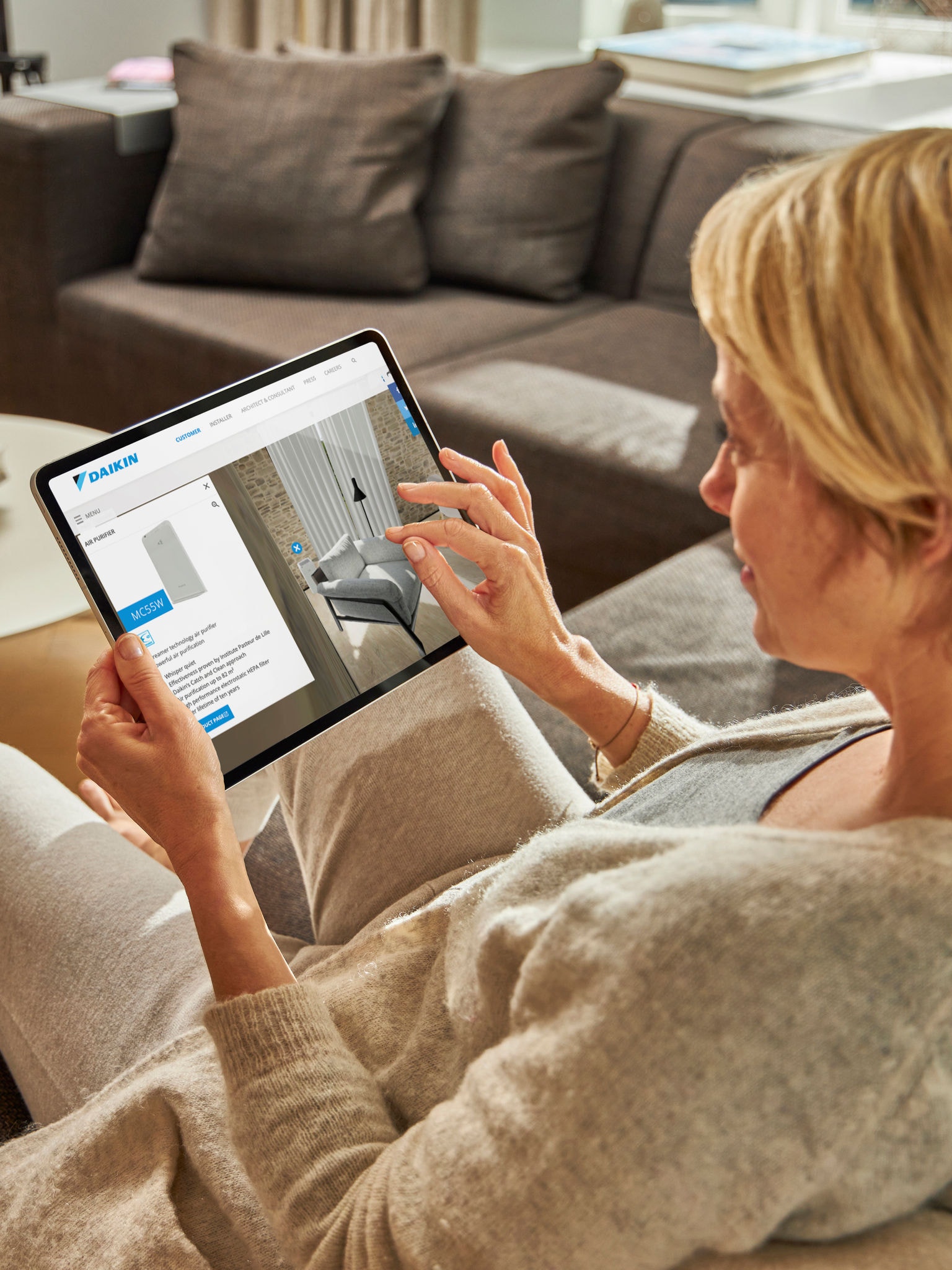 Eine Frau sitzt auf einem Sofa und betrachtet auf ihrem Tablet Luft-Wasser-Wärmepumpen im Virtual Experience Center