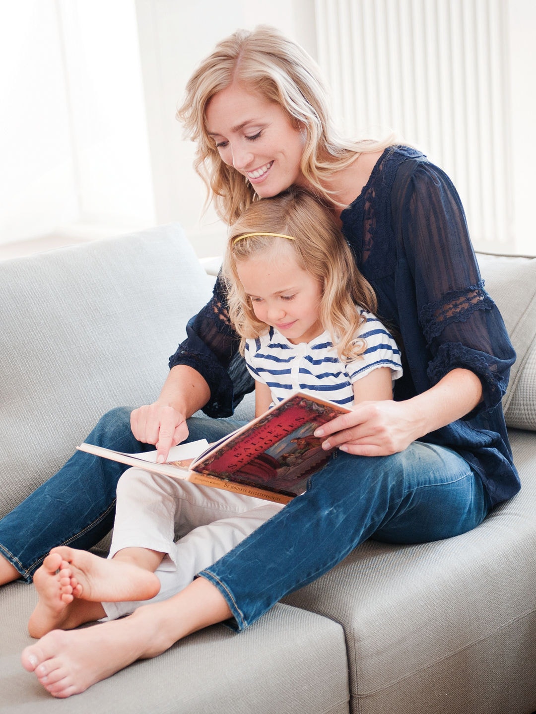 Eine Mutter schaut sich mit ihrer kleinen Tochter auf dem Schoß auf der Couch ein Buch an