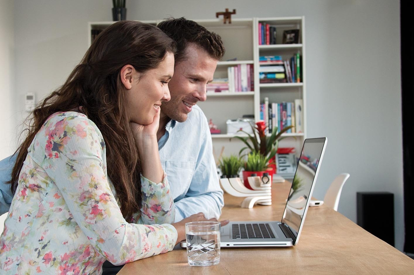 Ein Paar sitzt am Esstisch vor einem Laptop