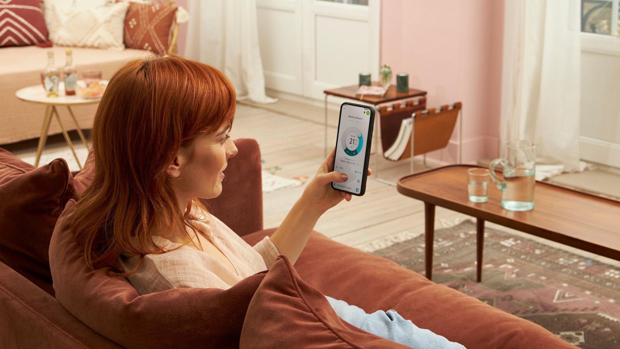 Eine Frau sitzt zu Hause auf einem Sofa und bedient die Onecta App auf ihrem Smartphone.