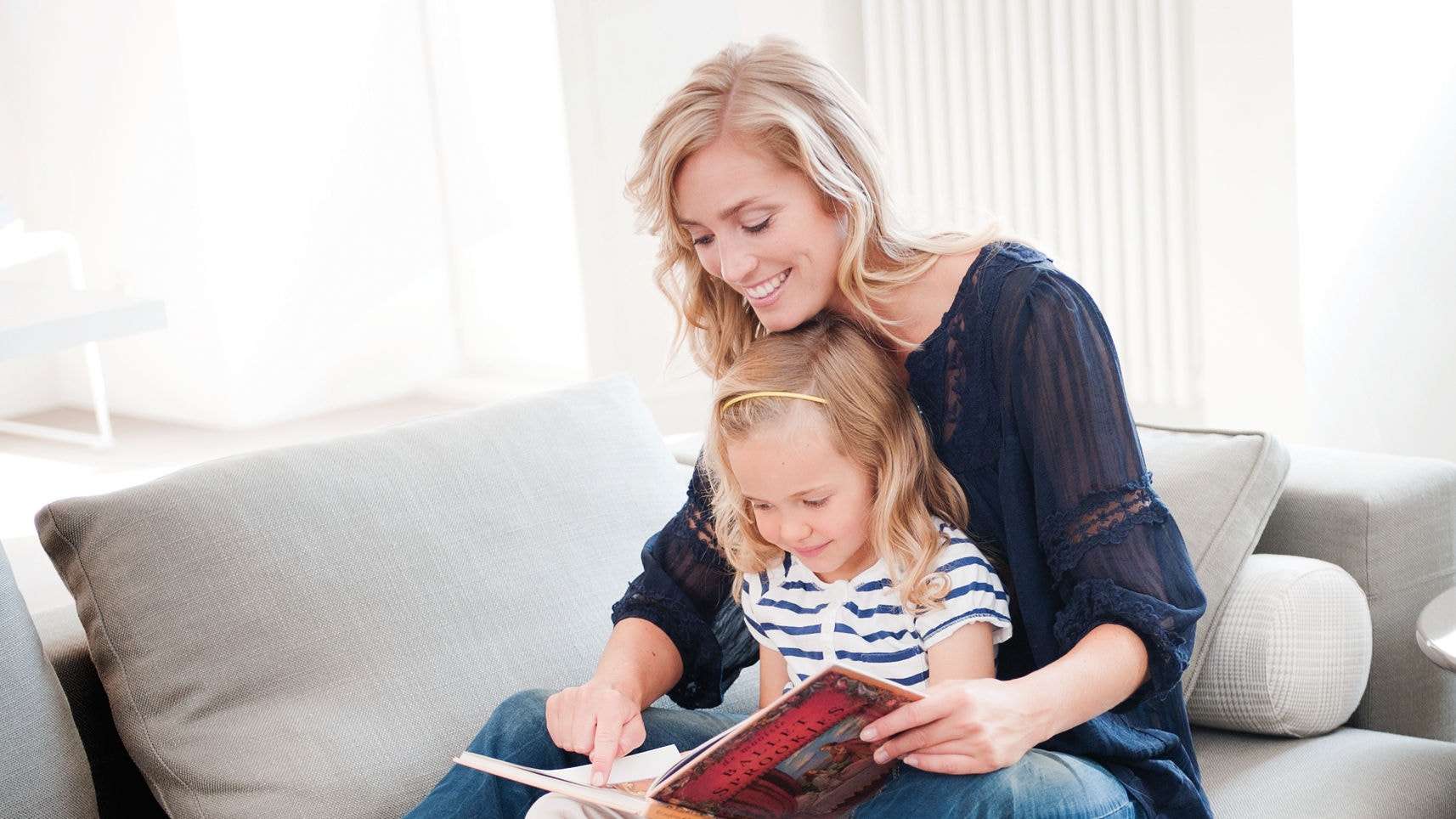 Mutter und Tochter lesen gemeinsam auf dem Sofa und genießen dabei das perfekte Raumklima