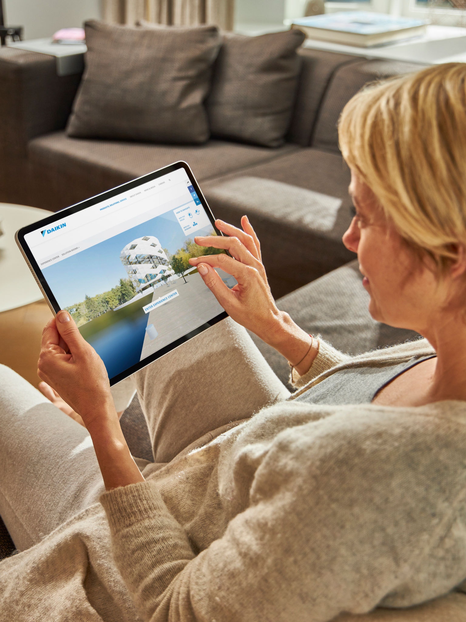 Eine Frau sitzt auf einem Sofa und betrachtet auf ihrem Tablet Luft-Wasser-Wärmepumpen im Virtual Experience Center