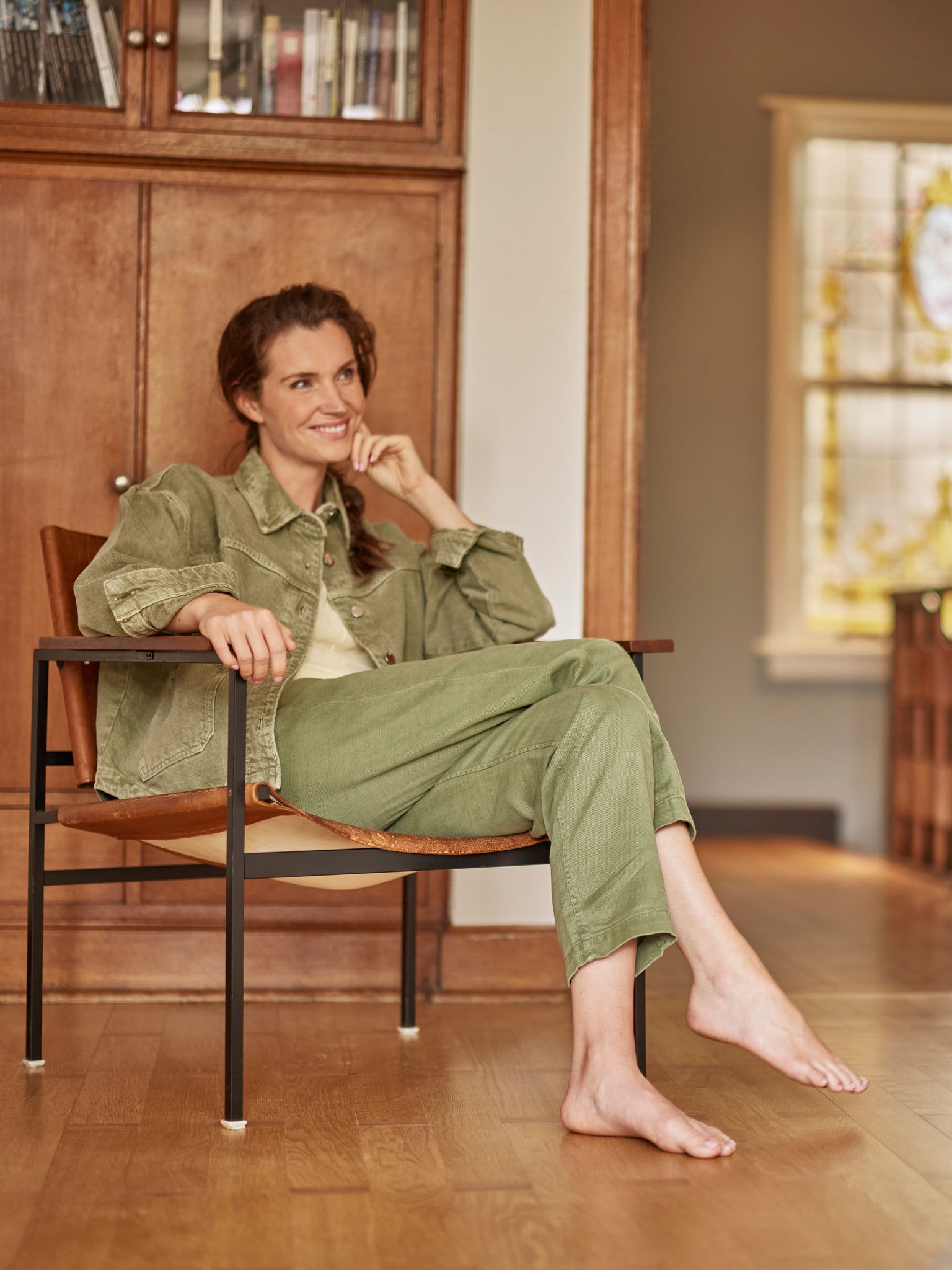 Frau sitzt barfuß im Sessel, lächelt und schaut nach oben