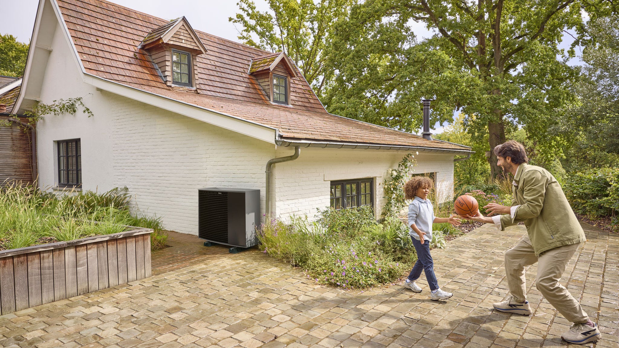 Vater spielt mit seinem Sohn Ball im Vorgarten eines Hauses