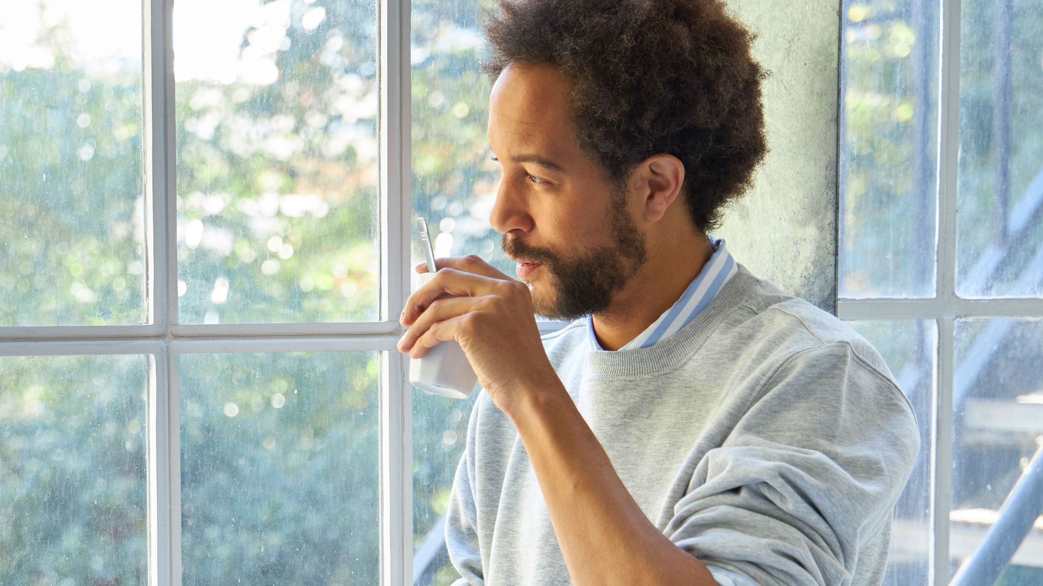 Bei Sonnenschein aus einer Tasse trinkender Mann neben einem Fenster
