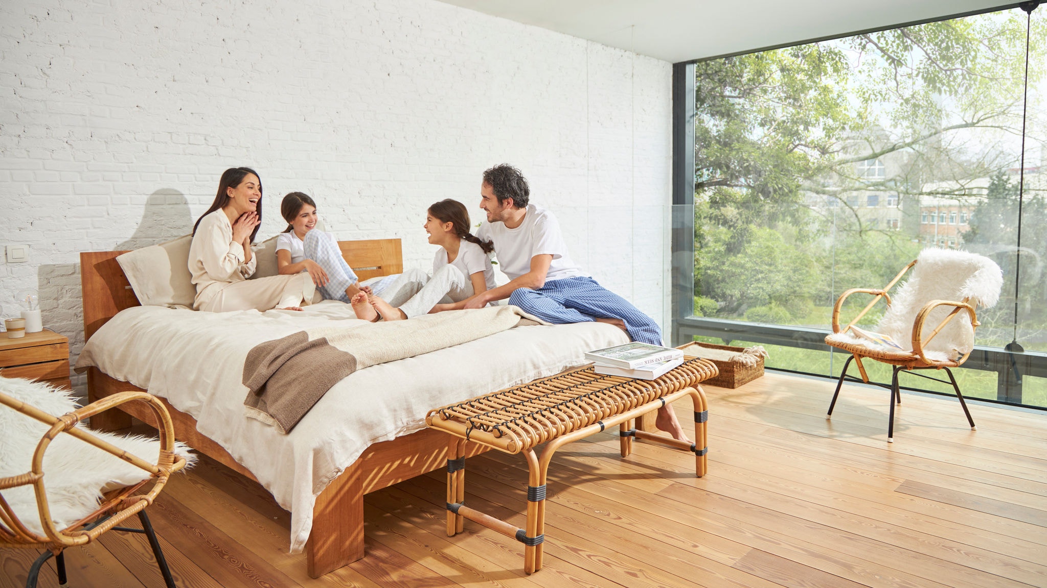 Eine Familie im Gespräch auf einem Bett in einem Schlafzimmer mit großer Glaswand, guter Raumluftqualität und viel natürlichem Licht
