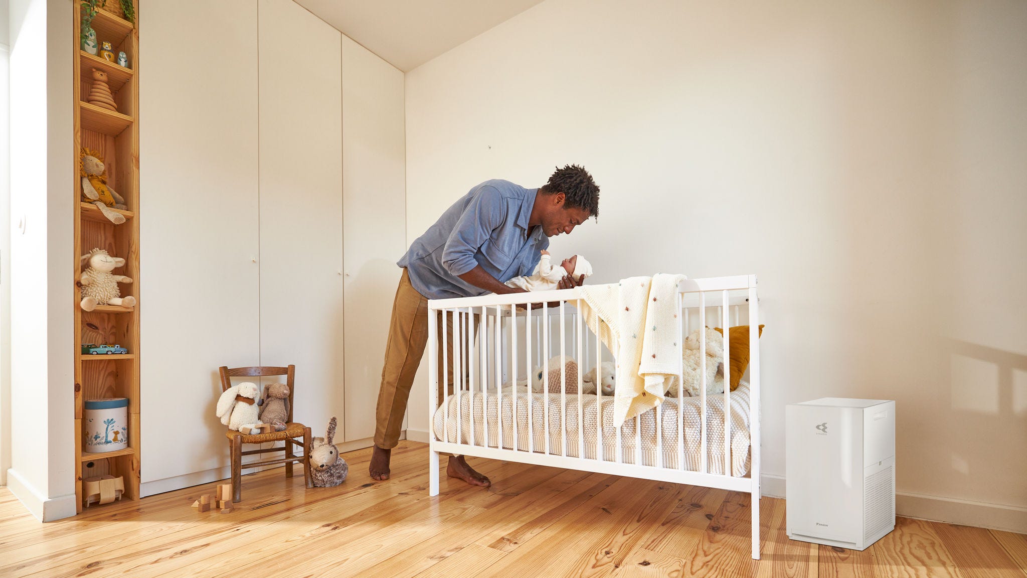 Ein Vater deckt sein Baby zu, in einem ruhigen Kinderzimmer mit einem Luftreiniger in der Nähe
