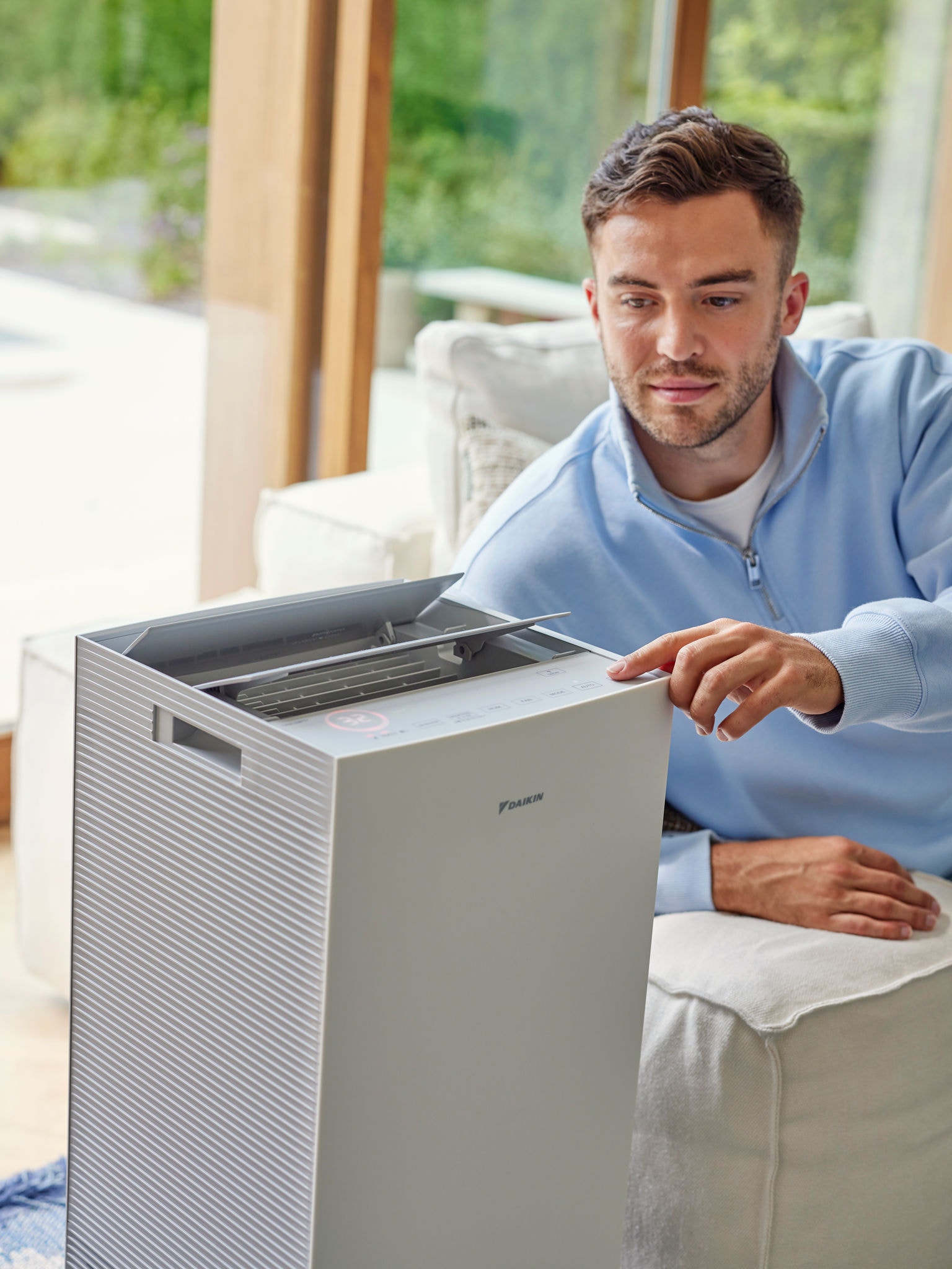 Ein Mann stellt einen Daikin Luftreiniger im Wohnzimmer ein, um Katzenallergene zu reduzieren
