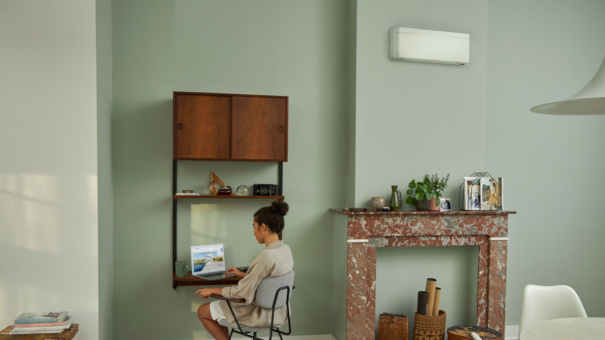 Eine an einem kleinen Tisch in einem hübschen Wohnzimmer sitzende Frau sieht sich über ihren Laptop im Daikin Virtual Experience Center um.